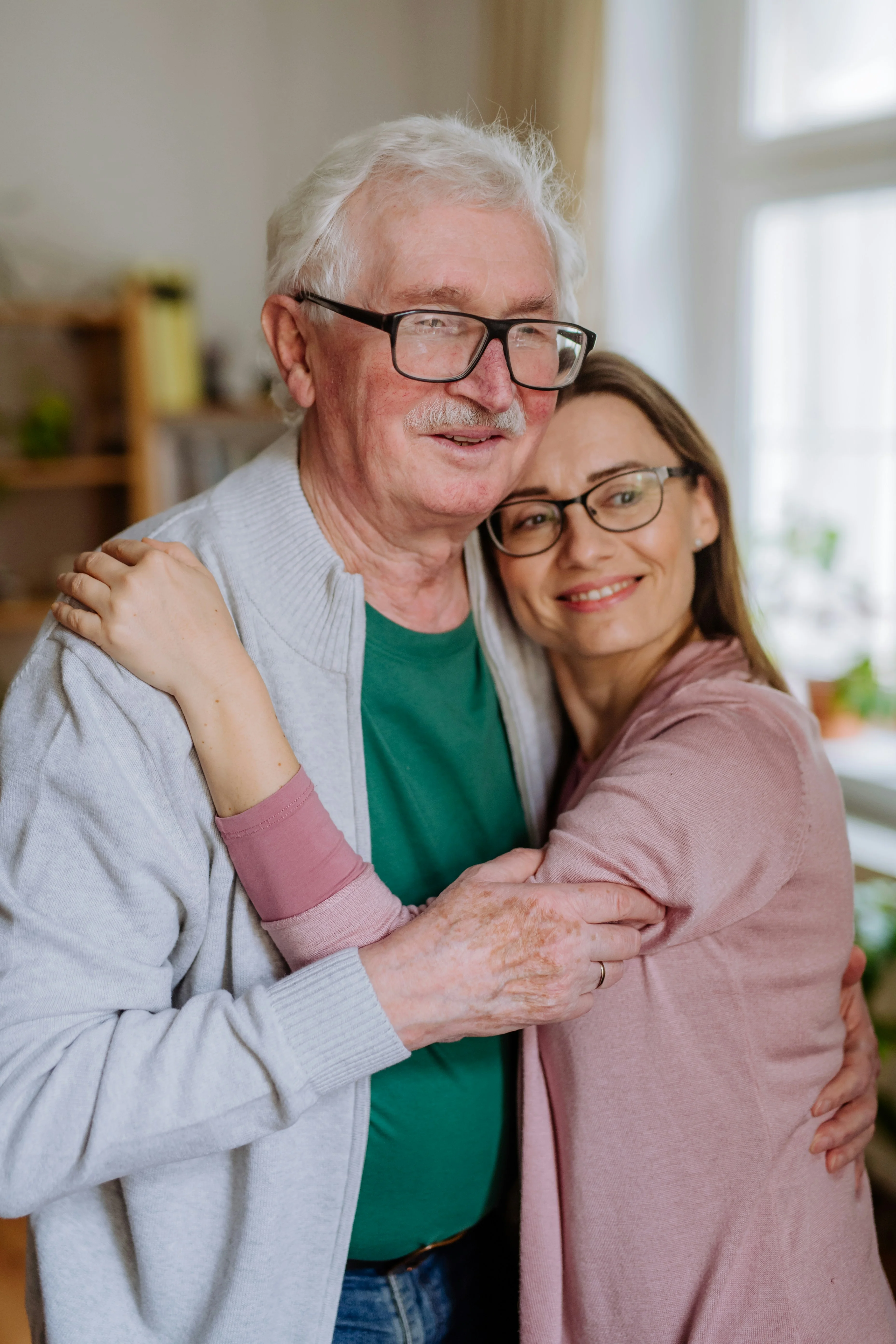 An elderly father and his adult daughter embracing warmly at home